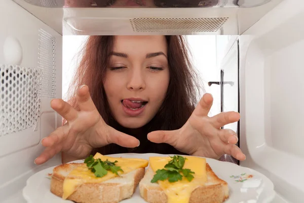 Attraktives Mädchen Schaut Auf Toasts Der Mikrowelle Und Leckt — Stockfoto