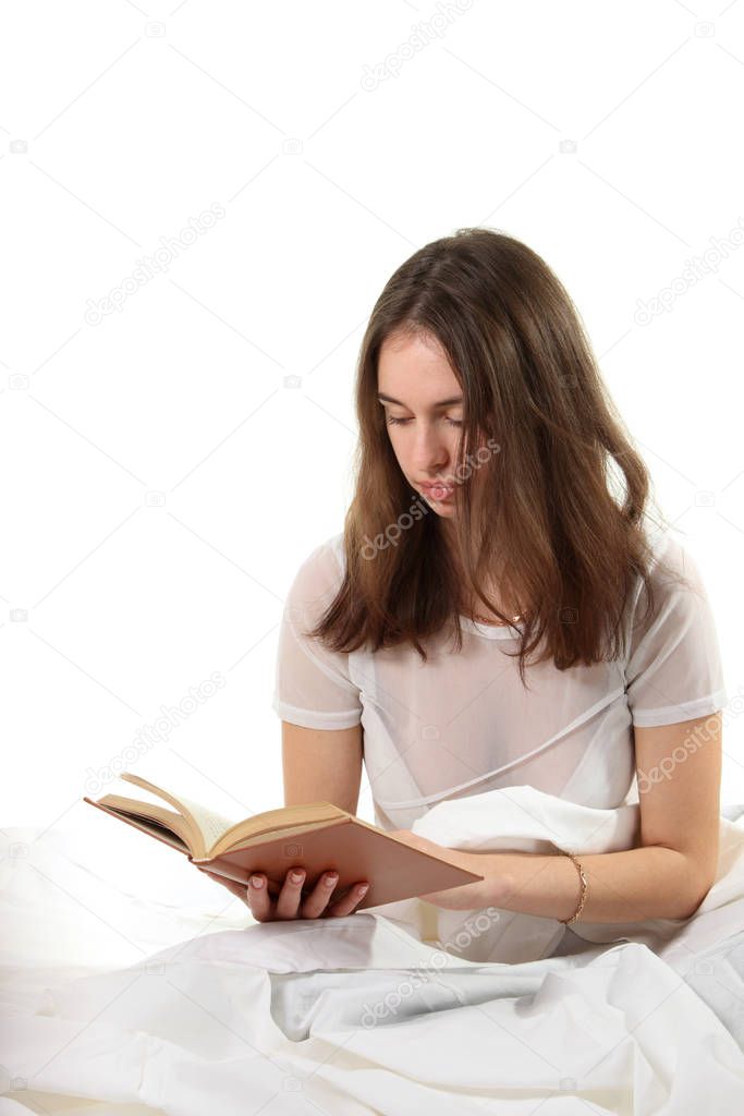 Young woman sitting in a bed and reading book
