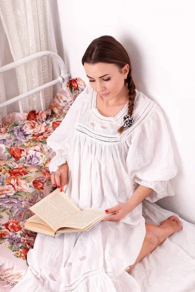 Young woman sitting in a bed and reading book