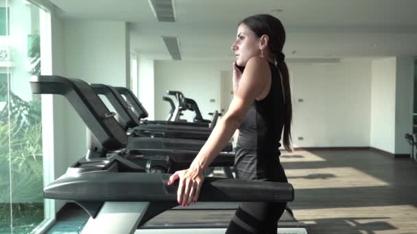 Atractiva chica asiática corriendo en la cinta de correr en el gimnasio. Chica hablando por teléfono — Vídeos de Stock