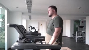 Sweaty fat man with a belly, walking on a treadmill, warming up on a treadmill