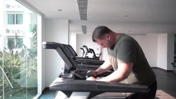Sweaty fat man with a belly, walking on a treadmill, warming up on a treadmill — Stok video