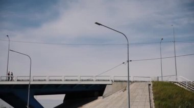 Mutlu çift, ekose gömlekler, el ele tutuşarak ve bir araba köprüde bir güneşli yaz gününde yürüyüş. Genel planı. Çok genel planı