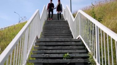 Mutlu çift, ekose gömlekler, el ele tutuşarak ve bir araba köprüde bir güneşli yaz gününde yürüyüş. Genel planı. Çok genel planı