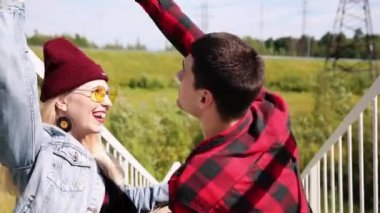 Mutlu çift, ekose gömlekler, el ele tutuşarak ve bir araba köprüde bir güneşli yaz gününde yürüyüş. Çift dans aşk. Köprü merdivenlerde otur, nazikçe birbirinize bakın. Yakın çekim