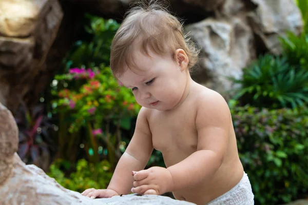 Jolie petite fille rampante souriante et rampante sur la passerelle brune en bois sur le fond de buissons et d'arbres verts. L'enfant trouvé sur le sol et essayant de manger. Il y a une place pour le texte . — Photo