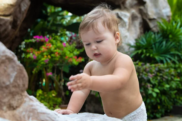 Jolie petite fille rampante souriante et rampante sur la passerelle brune en bois sur le fond de buissons et d'arbres verts. L'enfant trouvé sur le sol et essayant de manger. Il y a une place pour le texte . — Photo