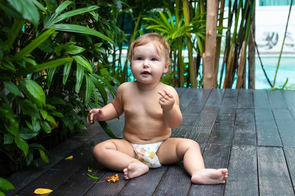 かなりクロール赤ちゃん女の子笑顔と緑の茂みや木の背景に木製の茶色の通路上でクロールします。子供と食べるしようと床の上します。テキストのための場所があります。. — ストック写真