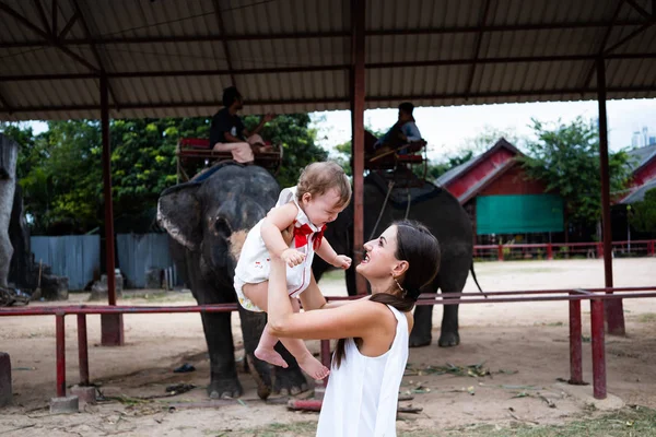 Mãe e filha felizes assistindo e alimentando elefantes no zoológico. Jovem mãe alimenta um elefante com sua filha, bebê alimenta um elefante — Fotografia de Stock