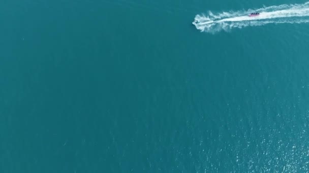 Vista superior, cámara lenta. moto de agua que pasa a través de la ola, rodando personas en la atracción del agua en el mar azul en la laguna azul . — Vídeo de stock