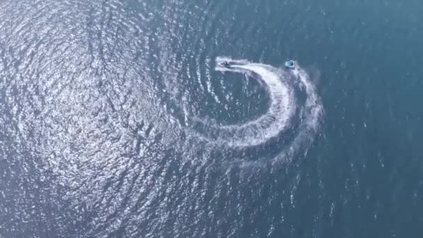 Вид зверху, повільний рух. водяний мотоцикл, що проходить крізь хвилю, прокочує людей на водному атракціоні на блакитному морі в синій лагуні . — стокове відео