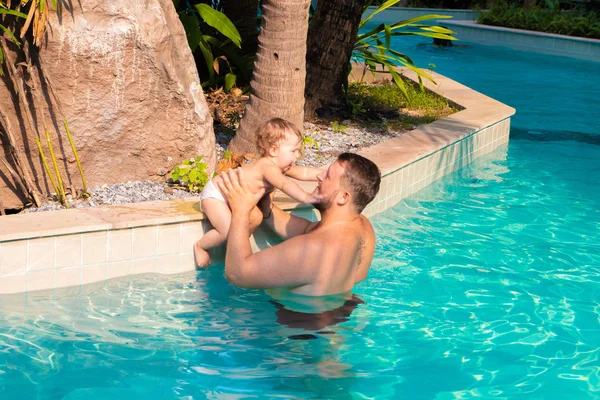 Dad teaches a child to swim in the pool. Father and child having fun in the pool. Dad and daughter swim in the pool on one of the palm trees. Father teaches daughter to swim. The concept of childrens