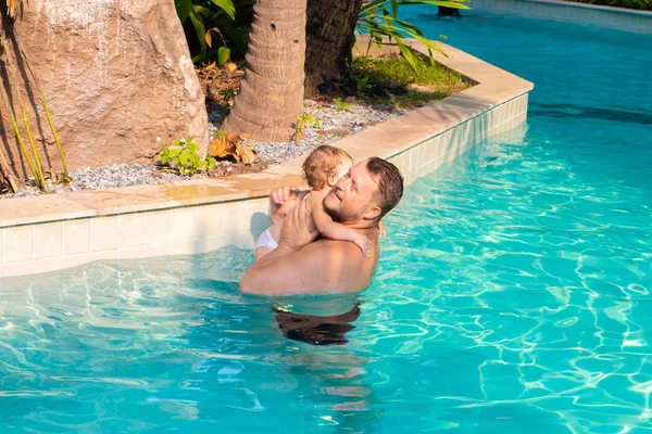 Dad teaches a child to swim in the pool. Father and child having fun in the pool. Dad and daughter swim in the pool on one of the palm trees. Father teaches daughter to swim. The concept of childrens