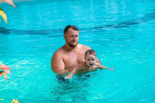 Isä opettaa lapsen uimaan altaassa. Isä ja lapsi pitävät hauskaa altaassa. Isä ja tytär uivat yhden palmun altaassa. Isä opettaa tytärtä uimaan. Lapsen käsite: — kuvapankkivalokuva