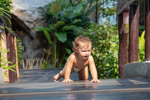 Funny baby learns to crawl. dynamic movement. child crawls along the dark brown wooden walkway of the bridge at sunset. A child learn to crawl. There is a place for text.