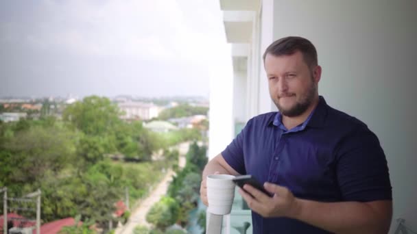 Uomo sul balcone che beve con una tazza e parla al telefono . — Video Stock