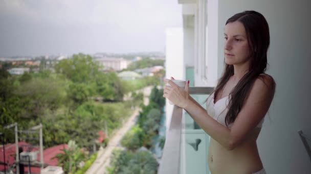 Девушка в нижнем белье на балконе пьет из кружки — стоковое видео