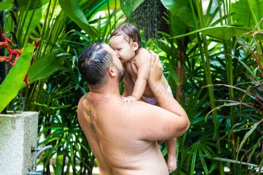 Baba ve bebek tropikal duş altında. Baba ve bebek duş su sıçramalarına altında sahilde oynarken