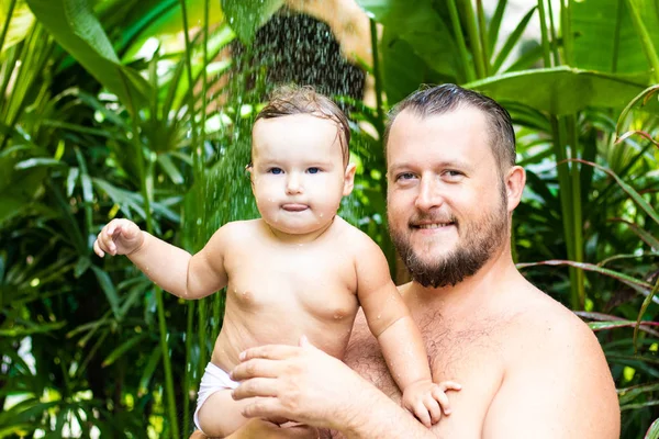 Papà e bambino sotto una doccia tropicale. papà e bambino giocare sulla spiaggia sotto doccia spruzzi d'acqua — Foto Stock