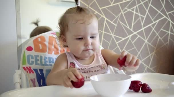 Aantrekkelijke baby eet aardbeien uit een witte plaat en is alle besmeurd met. Verse bessen. — Stockvideo