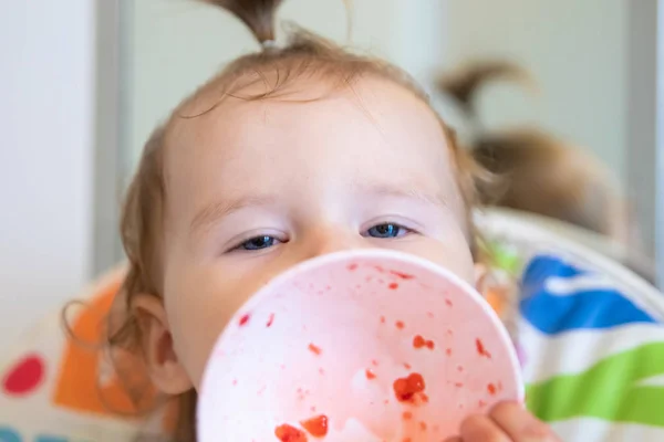 Attractive baby eats strawberries from a white plate and is all smeared with. Fresh berries. — Stock Photo, Image