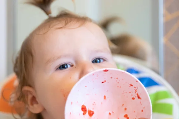 Ελκυστική μωρό τρώει φράουλες από μια λευκή πλάκα και είναι όλα smeared με. Φρέσκα μούρα. — Φωτογραφία Αρχείου