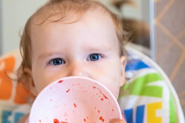 Atractivo bebé come fresas de un plato blanco y está todo untado con. Bayas frescas . — Foto de Stock