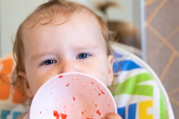 Atractivo bebé come fresas de un plato blanco y está todo untado con. Bayas frescas . — Foto de Stock