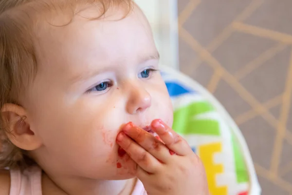 Cute little baby girl portrait funny eating red strawberries all smeared with — Stock Photo, Image