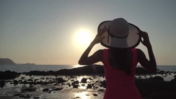 Chica en un sombrero pasea por la playa al atardecer — Vídeos de Stock