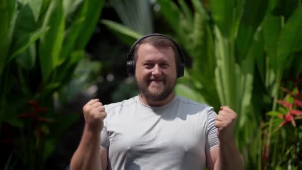 Bearded funny man puts on their clothes, turns on music, listens to energetic music, dances. Close-up — Stock Video