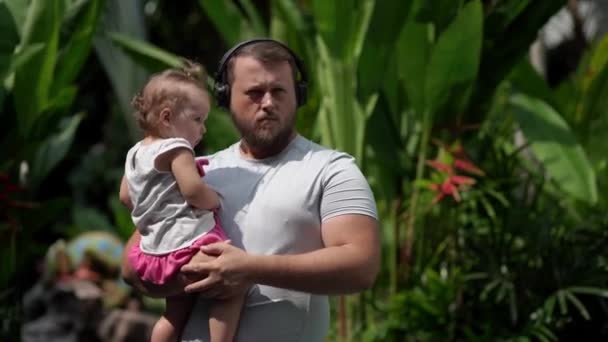 Mâle dans les écouteurs avec un enfant dans ses bras dans la rue se passe musique et danse. Gros plan — Video