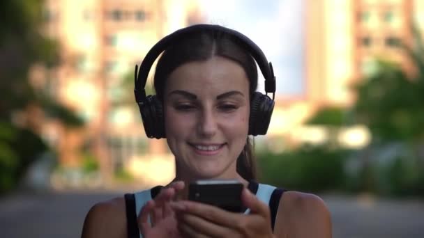 Dívka staví na sluchátka zahrnuje a poslouchá hudbu na telefonu a tanec. detail. 4k — Stock video