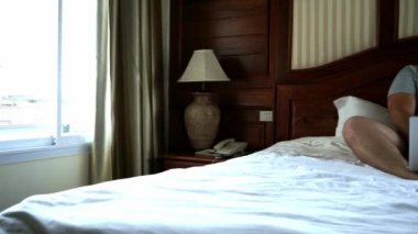 Yatağın üstüne oturan ve dizüstü bilgisayarda çalışan genç erkek. 4k.