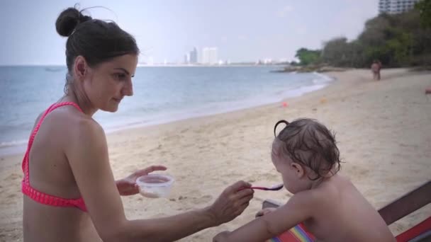 Mutter füttert ihre Tochter am Strand mit einem Löffel. Nahaufnahme. 4k. — Stockvideo