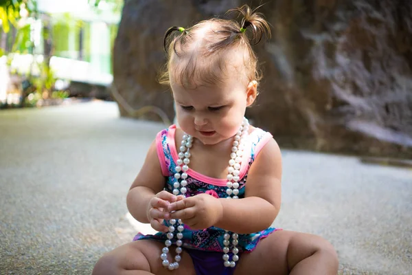 Une fille en maillot de bain avec des perles blanches est surprise, se réjouit, crie, lève les mains. concept de mode pour enfants . — Photo