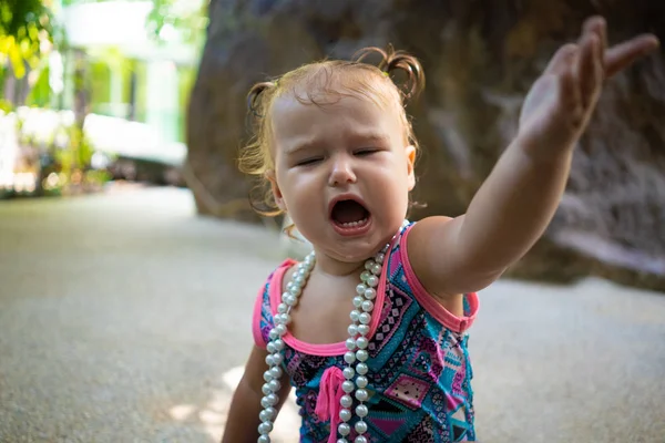 Una ragazza in costume da bagno con perline bianche è sorpresa, gioisce, grida, alza le mani. concetto di moda per bambini . — Foto Stock