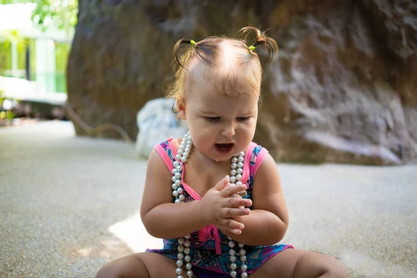 Uma menina em um maiô com contas brancas é surpreendida, se alegra, grita, levanta as mãos. conceito de moda infantil . — Fotografia de Stock