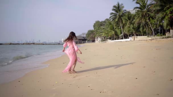 Hermosa hembra en un largo vestido rosa en desarrollo paseos caminando alrededor girando en la playa en las rocas. Primer plano. 4k . — Vídeo de stock