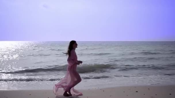 Beautiful female in a long developing pink dress walks walking around spinning on the beach on the rocks. close-up. 4k. — Stock Video