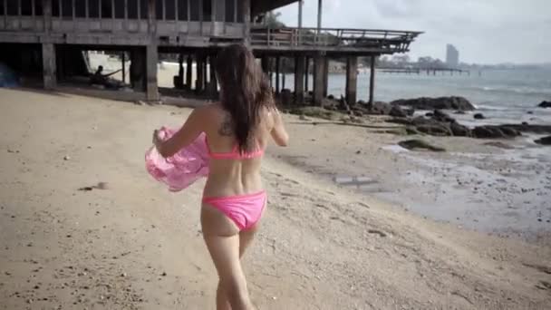 Bella femmina in un lungo vestito rosa in via di sviluppo cammina girando sulla spiaggia sulle rocce. primo piano. 4k . — Video Stock