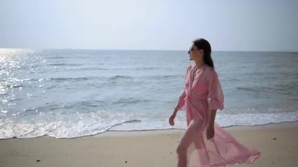 Hermosa hembra en un largo vestido rosa en desarrollo paseos caminando alrededor girando en la playa en las rocas. Primer plano. 4k . — Vídeos de Stock