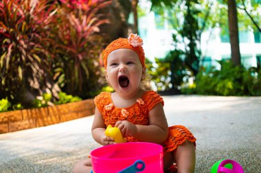 bir kız bir turuncu örme elbise ve şapka şaşırır, sevinir, bağırır, ağlar, elleri yükseltir. Çocuk moda kavramı.