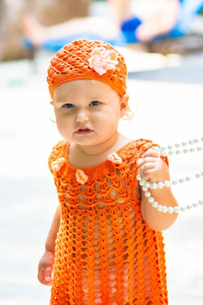 Uma menina em um vestido de malha laranja e chapéu é surpreendida, se alegra, grita, chora, levanta as mãos. conceito de moda infantil . — Fotografia de Stock