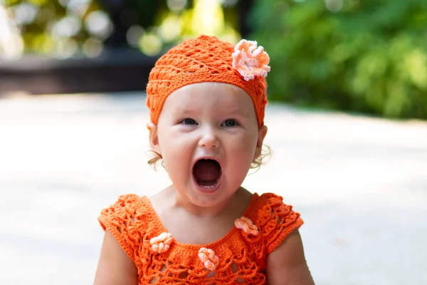 Een meisje in een oranje gebreide jurk en muts is verbaasd verheugt zich, gilt, huilt, werpt haar handen. Childrens mode concept. — Stockfoto