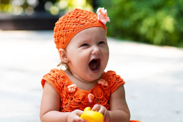 Een meisje in een oranje gebreide jurk en muts is verbaasd verheugt zich, gilt, huilt, werpt haar handen. Childrens mode concept. — Stockfoto