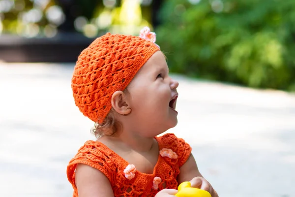 Dívka v oranžové pletené šaty a klobouk je překvapený, raduje se, křičí, pláče, vyvolává její ruce. dětské módní koncept. — Stock fotografie