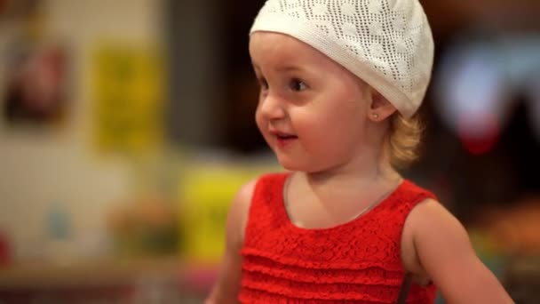 Menina de dois anos em um vestido vermelho e chapéu branco é alegre, retrato, close-up. 4k — Vídeo de Stock