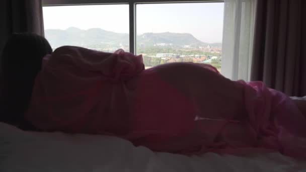 Kadın bir pembe şeffaf sabahlık yatakta yatıyor ve panoramik penceresinin içine bakıyor ve kahve içiyor. 4 k Hua Hin, Tayland — Stok video