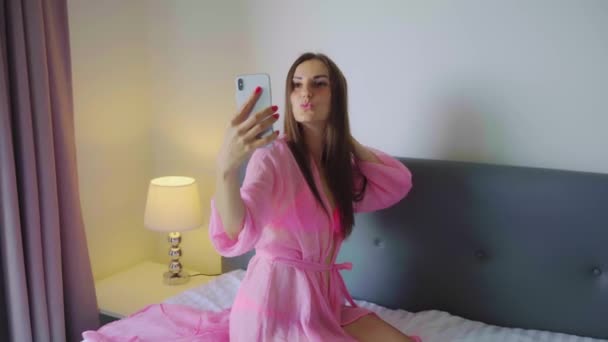 Chica en una túnica rosa transparente hace selfie en la cama. 4k . — Vídeos de Stock